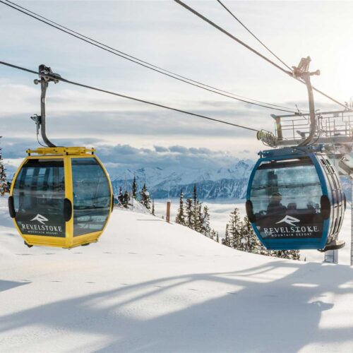 Yellow and blue gondola cars at Revelstoke Mountain Resort with snowy peaks in the background.
