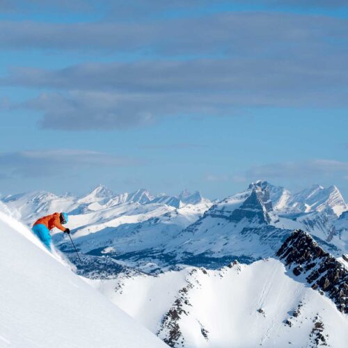 A skier in an orange jacket and blue pants skiing at Lake Louise Ski Resort in the Canadian Rockies.