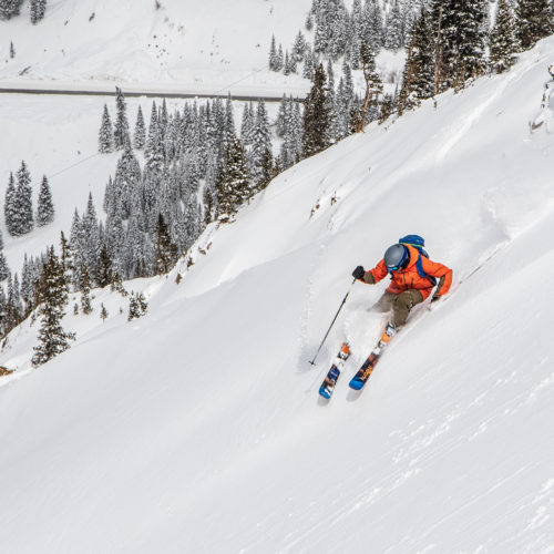 Un skieur vêtu d'une veste orange skiant sur une pente raide à Arapahoe Basin au Colorado avec un Mountain Collective passer.