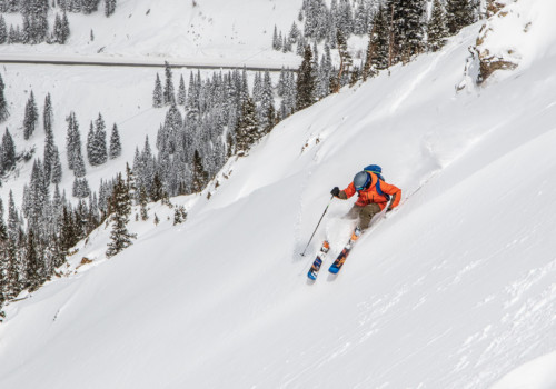 Un skieur vêtu d'une veste orange skiant sur une pente raide à Arapahoe Basin au Colorado avec un Mountain Collective passer.