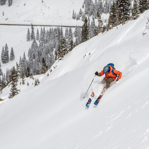 A skier in an orange jacket skiing a steep slope at Arapahoe Basin in Colorado with a Mountain Collective pass.