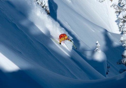 Un skieur portant une veste jaune et un sac à dos rouge skiant de la poudreuse à Alta Ski Area avec Mountain Collective.