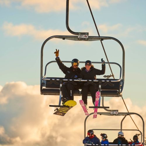 A snowboarder and skiier smiling while riding the chairlift at Mt Buller in Australia.