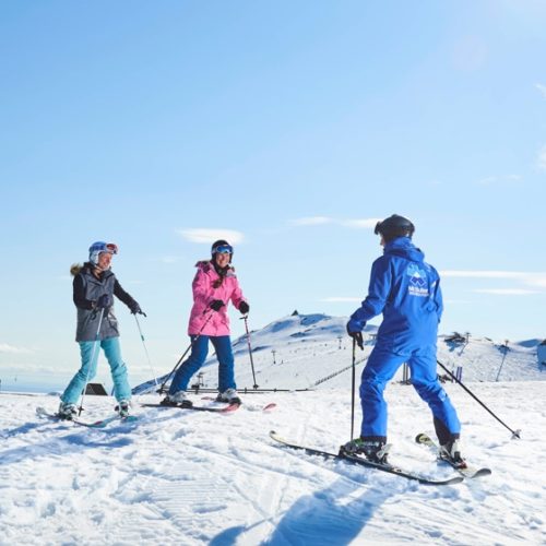 Two women smiling with a ski instructor while taking ski lessons at Mt Buller in Australia.