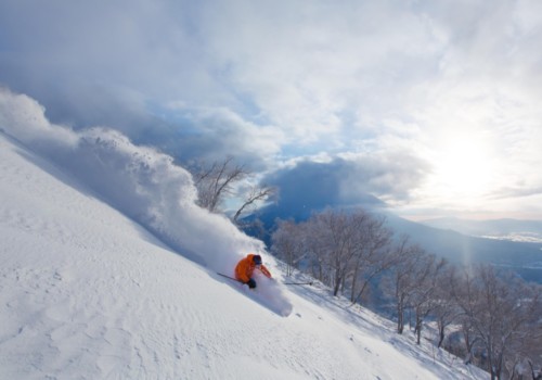 A skier in an orange jacket skiing through fresh powder at Niseko in Japan with Mountain Collective.