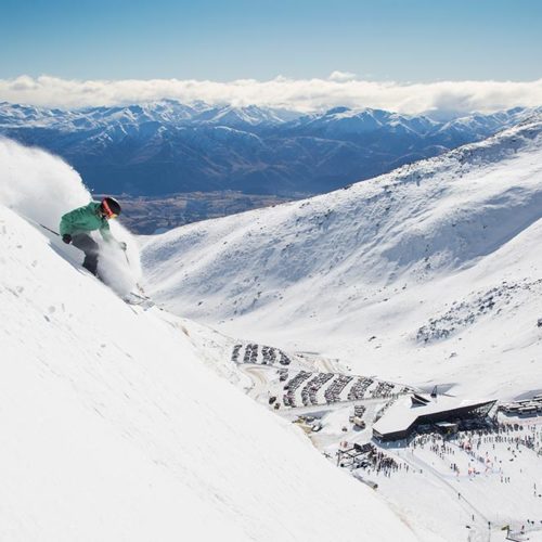 A skier in a teal jacket skiing a steep slope at Coronet Peak + The Remarkables in NZ.