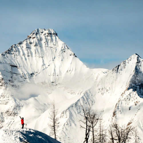 A skier in a red jacket looking at two steep peaks at Panorama Mountain Resort in Canada.