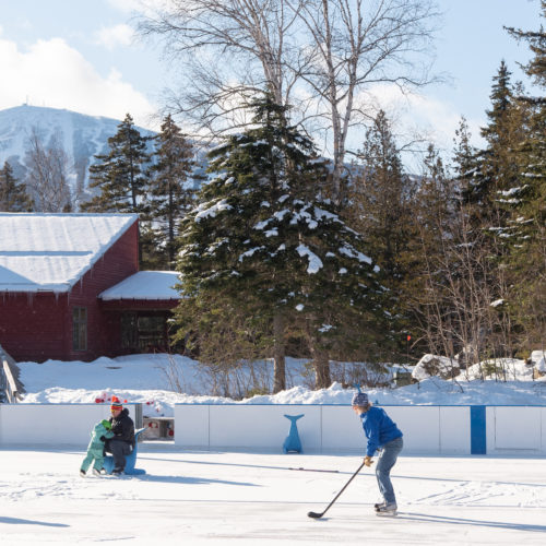 A family playing ice hockey at Sugarloaf with views of the ski slopes in the background.