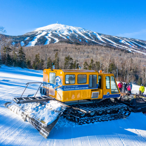 Une machine à chat jaune se préparant à emmener un groupe de skieurs sur les pistes de Sugarloaf pour une véritable expérience de cat ski en Nouvelle-Angleterre