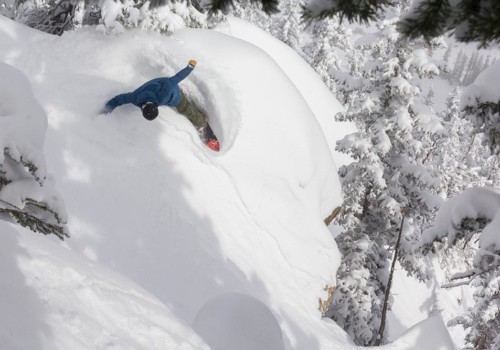 A snowboarder in a blue jacket carving a powder pillow through pine trees at Taos Ski Valley in New Mexico with Mountain Collective.
