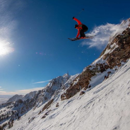 A skier in a red & black jacket getting big air on the slopes of Snowbasin in Utah.