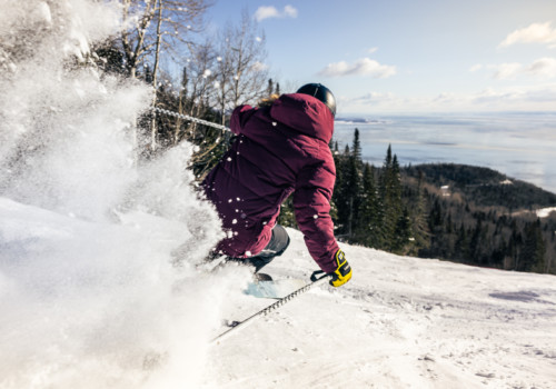 A skier in a maroon jacket carving the slopes of Le Massif in Canada with Mountain Collective.