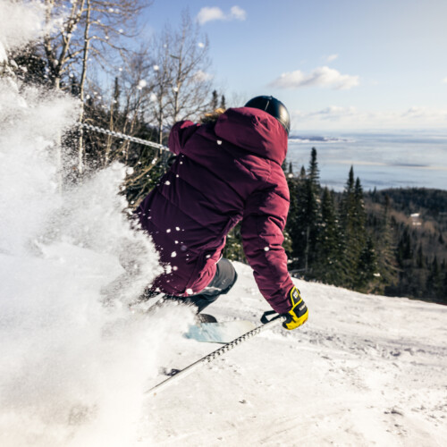 Un skieur vêtu d'une veste marron dévalant les pentes du Massif au Canada avec Mountain Collective.