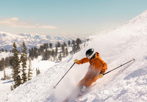 A skier in an orange snowsuit with poles going down a mountain