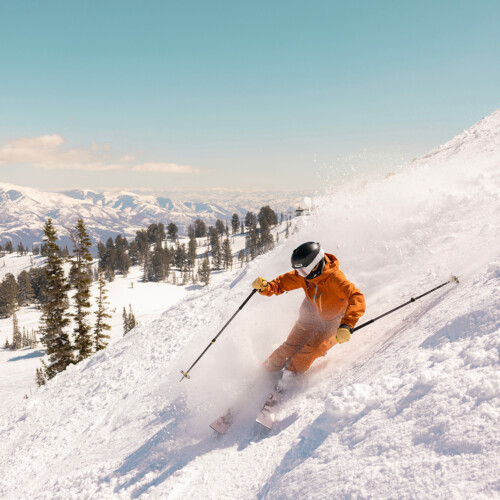 Un skieur en habit de neige orange avec des bâtons descendant une montagne